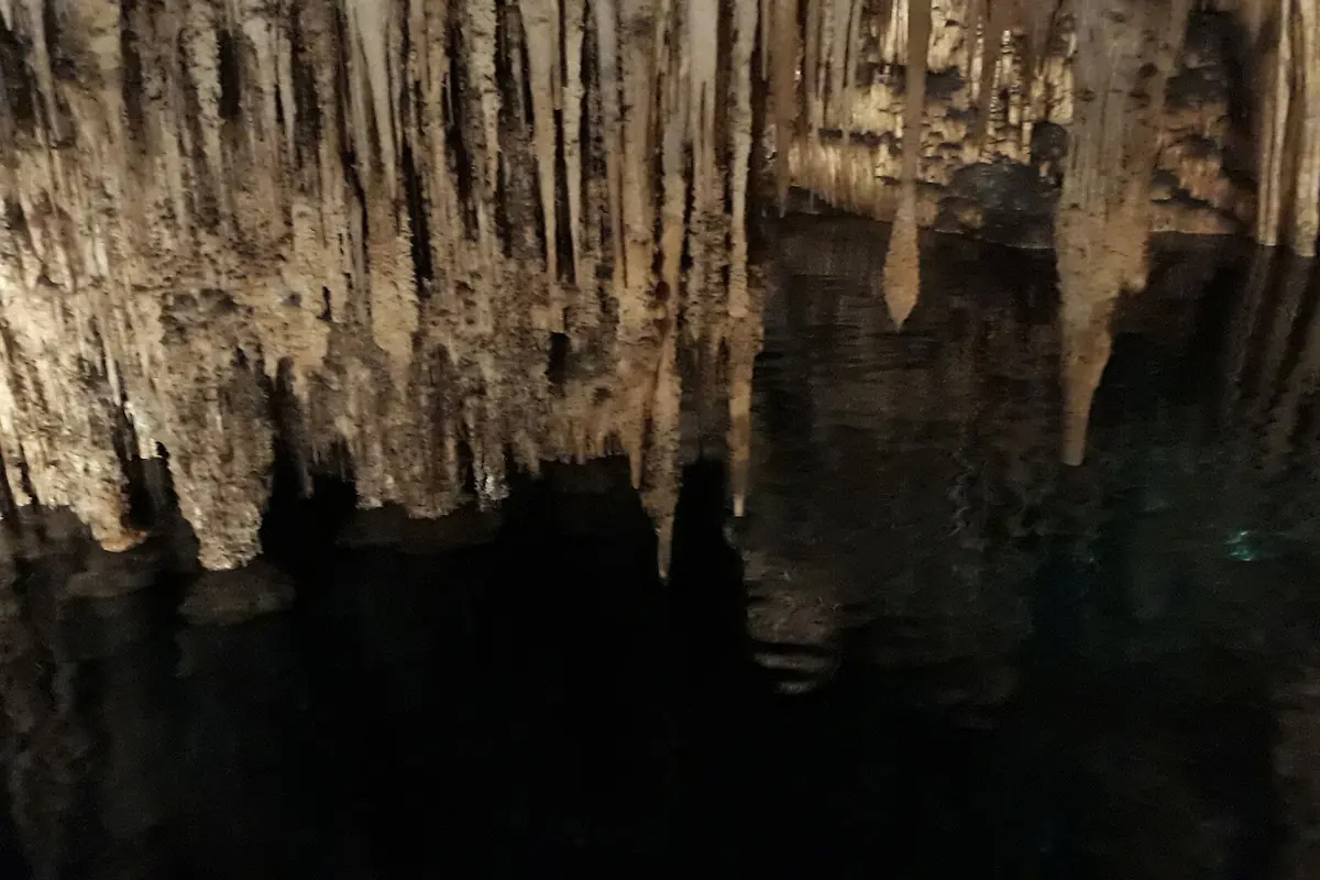 Stalaktity visící nad klidnou tmavou vodou jezera Martel, jejich špičky se odrážejí na hladině.